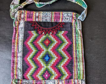 May include: A small, colourful, woven crossbody bag with a zipper closure and a fringe trim. The bag features a geometric pattern in shades of pink, green, blue, and white.