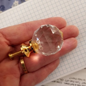 May include: A clear glass crystal cabinet knob with a gold metal base and screw. The knob has a faceted design.