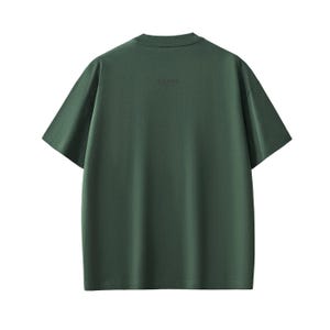 Pu&ograve; includere: Una maglietta verde scuro a maniche corte. La parola "DAFFA" &egrave; stampata in modo discreto sul retro della maglietta, vicino allo scollo. La maglietta ha un design semplice e classico.