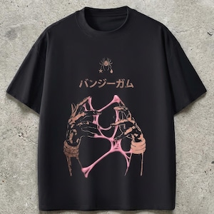 Pu&ograve; includere: T-shirt nera con un design grafico raffigurante mani e una sostanza rosa appiccicosa. Il testo giapponese "バンジーガム" &egrave; sopra la grafica. Una piccola grafica di ragno e stella &egrave; sopra il testo.