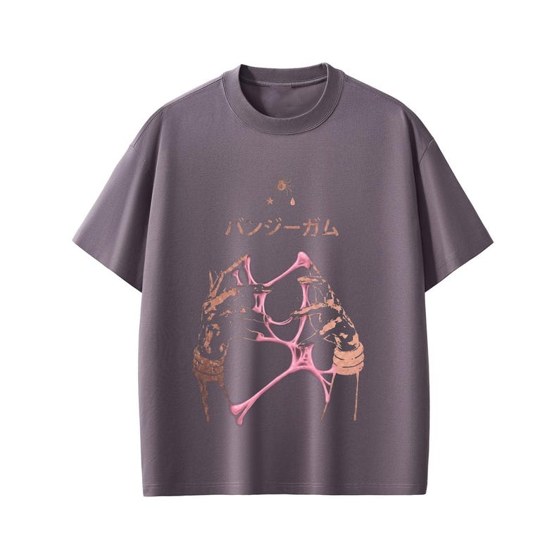 Pu&ograve; includere: T-shirt grigio a maniche corte e girocollo. La parte anteriore presenta un design grafico di mani con elementi rosa e marroni e testo giapponese. Il design include stelle e una goccia.