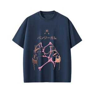 Pu&ograve; includere: T-shirt blu navy con scollo tondo e design grafico. Il design presenta un'illustrazione stilizzata di mani che tengono una sostanza rosa e appiccicosa, con testo giapponese e una piccola illustrazione di stella e ragno.
