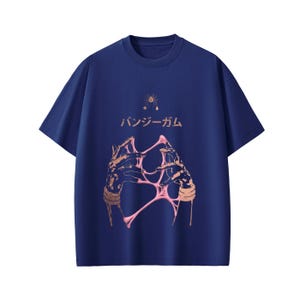 Pu&ograve; includere: T-shirt blu navy con un design grafico. Il design include il testo giapponese "バンジーガム", un'illustrazione stilizzata di mani e materiale rosa appiccicoso, una stella e un grafico di ragno.