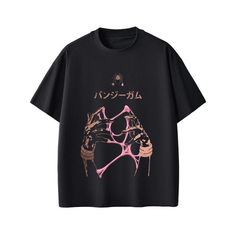 Pu&ograve; includere: T-shirt nera con un design grafico che presenta mani e materiale rosa appiccicoso. Il testo giapponese "バンジーガム" &egrave; sopra le mani e una piccola grafica di ragno &egrave; nella parte superiore.
