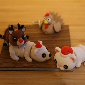 May include: A set of four Christmas-themed figurines: a reindeer, a polar bear, a cat, and a turkey. The figurines are made of a soft, pliable material and are painted in bright, festive colors.