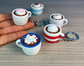 May include: Five miniature ceramic mugs with different colored stripes and toppings, including whipped cream, sprinkles, and marshmallows, attached to key rings. The mugs are arranged on a wooden surface.