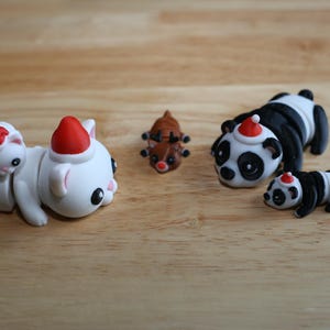 May include: A set of five Christmas-themed animal figurines. The figurines are made of white, black, and brown plastic. They include a panda, a reindeer, and three cats wearing Santa hats.