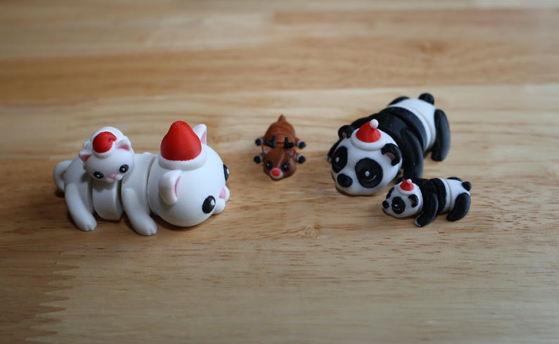 May include: A set of five Christmas-themed animal figurines. The figurines are made of white, black, and brown plastic. They include a panda, a reindeer, and three cats wearing Santa hats.