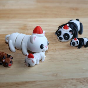May include: Five small, white, and black animal figurines wearing Santa hats. The figurines are a cat, a reindeer, a panda, and two baby pandas.