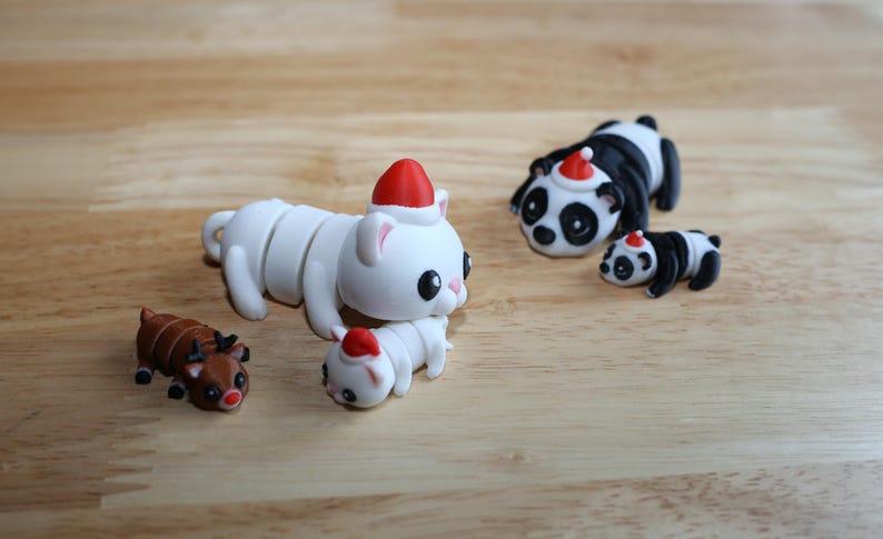 May include: Five small, white, and black animal figurines wearing Santa hats. The figurines are a cat, a reindeer, a panda, and two baby pandas.