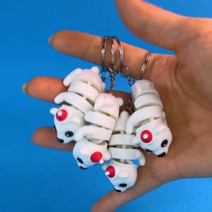 May include: Four white skeleton dog keychains with red accents. The keychains are attached to a silver keyring.