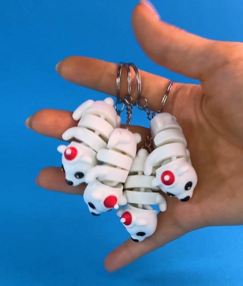 May include: Four white skeleton dog keychains with red accents. The keychains are attached to a silver keyring.