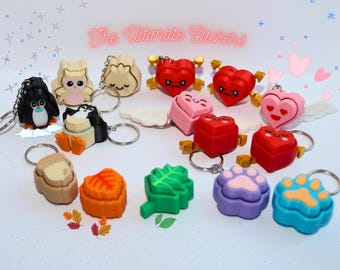 May include: A collection of 12 colorful keychains featuring various designs, including owls, penguins, hearts, acorns, leaves, and paw prints. The keychains are made of a soft, squishy material and have a clicker mechanism. The text "The Ultimate Clickers" is displayed at the top of the image.