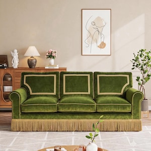 May include: A three-cushion sofa upholstered in deep green velvet fabric, featuring light gold piping accents along the cushions and backrest, and a long, decorative gold fringe trim along the bottom edge of the base frame.