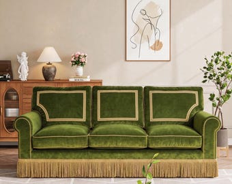 May include: A three-cushion sofa upholstered in deep green velvet fabric, featuring light gold piping accents along the cushions and backrest, and a long, decorative gold fringe trim along the bottom edge of the base frame.