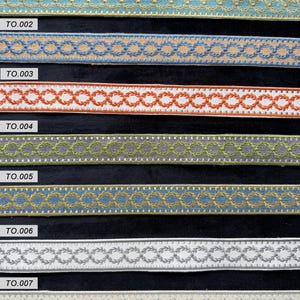 May include: Seven horizontal strips of decorative woven trim, each featuring a repeating embroidered laurel wreath chain pattern. The strips are labeled TO.001 through TO.007 and display various color combinations including blue, tan, orange, white, green, and grey.