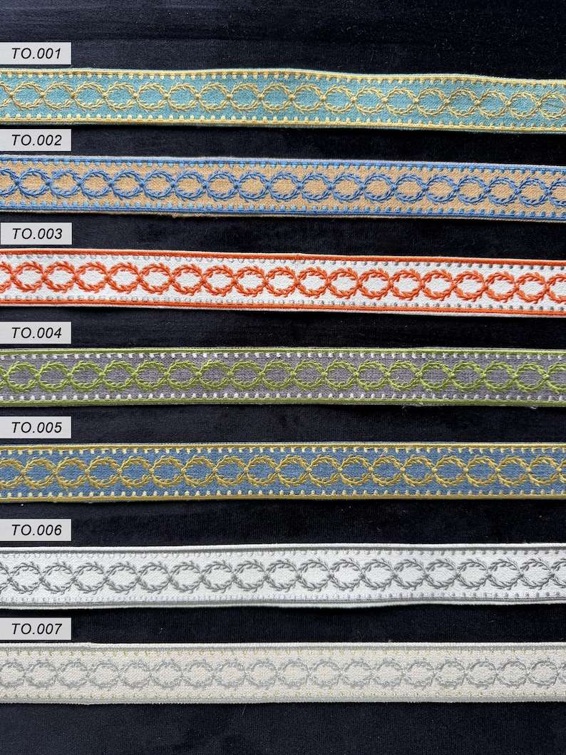 May include: Seven horizontal strips of decorative woven trim, each featuring a repeating embroidered laurel wreath chain pattern. The strips are labeled TO.001 through TO.007 and display various color combinations including blue, tan, orange, white, green, and grey.