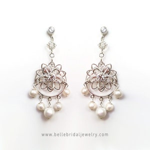 Puede incluir: Pendientes de aro de plata con un dise&ntilde;o floral y detalles de perlas. Los pendientes presentan una delicada flor calada con un centro de cristal transparente y una fila de perlas que cuelgan debajo.