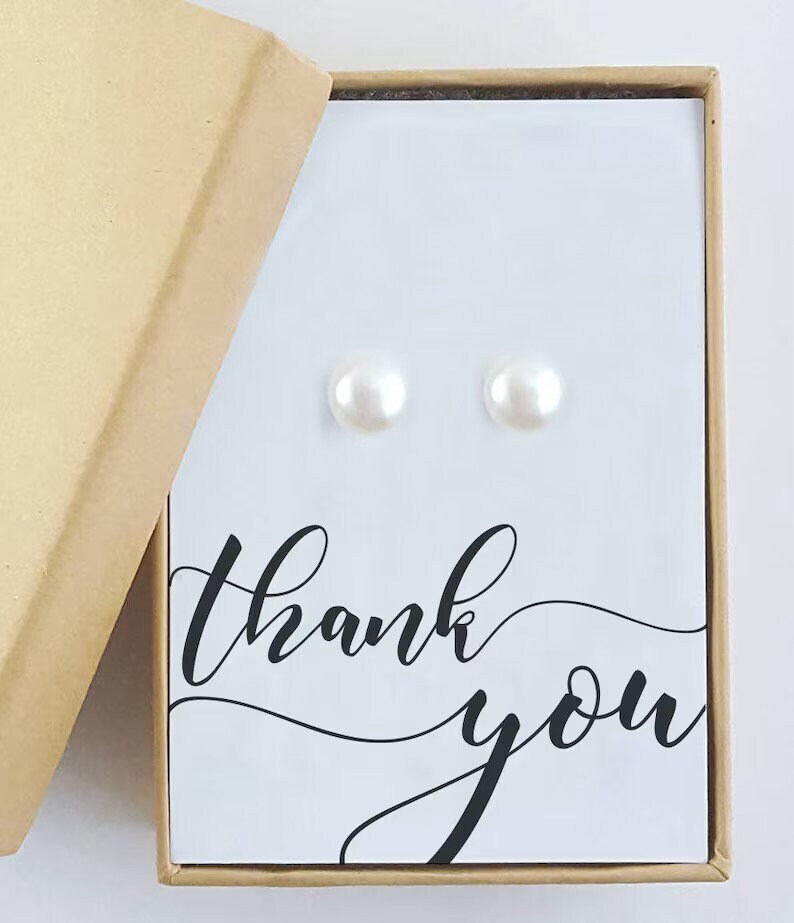 May include: A small, white gift box with a thank you message on the front. The box is open and contains a pair of pearl earrings.