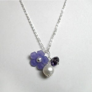 May include: A silver chain necklace with a purple flower charm, a small purple crystal, and a white pearl.
