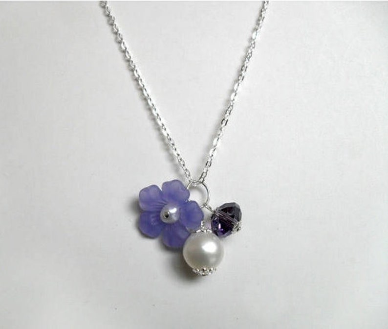 May include: A silver chain necklace with a purple flower charm, a small purple crystal, and a white pearl.