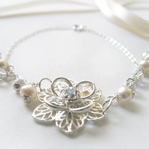 Puede incluir: Un collar de plata con un delicado colgante de flor y detalles de perlas y cristales.