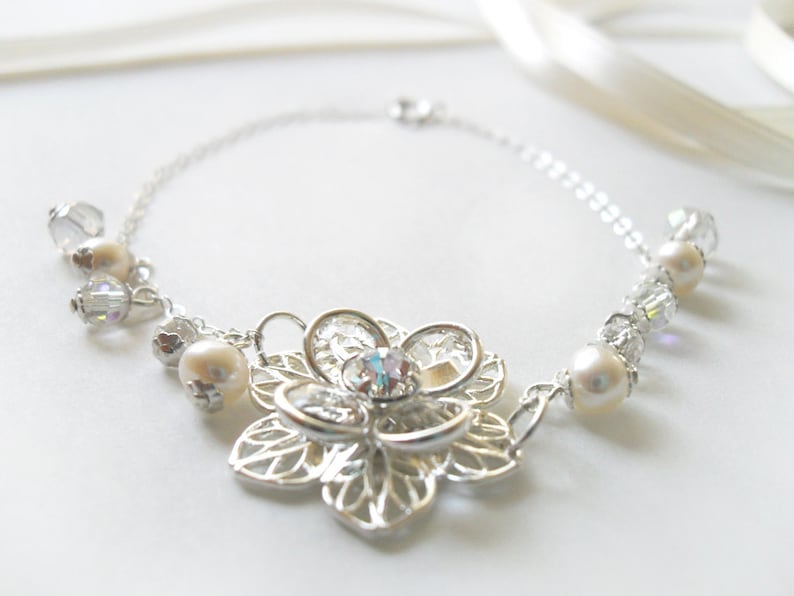Puede incluir: Un collar de plata con un delicado colgante de flor y detalles de perlas y cristales.