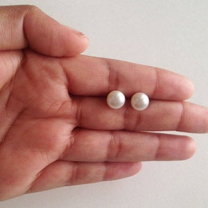 May include: A pair of white pearl stud earrings. The earrings are small and round, and they are set in a silver metal setting.