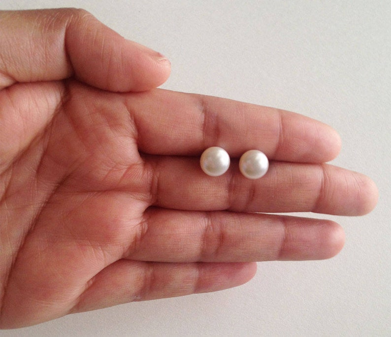 May include: A pair of white pearl stud earrings. The earrings are small and round, and they are set in a silver metal setting.
