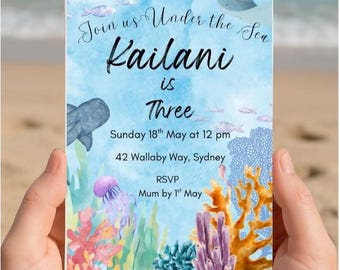 May include: An invitation with an underwater theme, held by hands. The invitation reads "Join us Under the Sea Kailani is Three" with event details. Colorful coral, fish, and a jellyfish decorate the card.