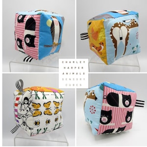 May include: Four Charley Harper Animals Sensory Cubes. Each cube features colorful animal illustrations on various fabric panels. The cubes have black and white striped or solid color pull tabs. The cubes are displayed on clear acrylic stands.