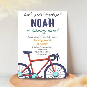 May include: A white invitation card with the text "Let's pedal together!" and "NOAH is turning nine!" in navy blue. A red bicycle illustration is featured below the text, with details in blue and light blue. The invitation includes party details.