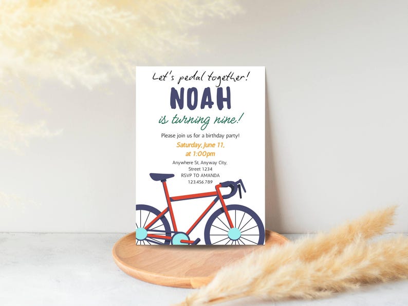 May include: A white invitation card with the text "Let's pedal together!" and "NOAH is turning nine!" in navy blue. A red bicycle illustration is featured below the text, with details in blue and light blue. The invitation includes party details.
