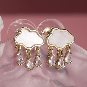 Puede incluir: Un par de pendientes de oro con un diseño de nube blanca y gotas de cristal transparente colgantes.