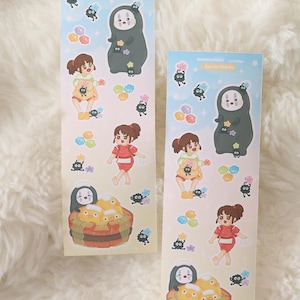 May include: Two decorative stickers featuring characters from "Spirited Away." The stickers have a light blue background with illustrations of characters, including No-Face, Chihiro, and soot sprites. The stickers are rectangular and have Japanese text at the top.