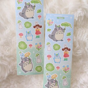 May include: Two sticker sheets with Totoro characters on a pale blue backdrop. The stickers depict Totoro, a girl in a red dress, and forest-themed illustrations. The text "Totoro" is printed on the sheets.