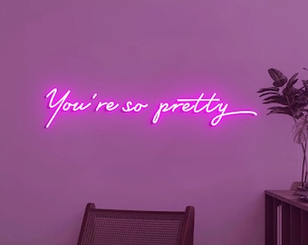 May include: Pink neon sign with the text "You're so pretty" on a purple wall.