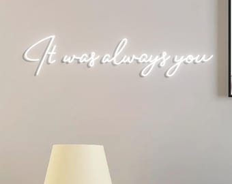 May include: White neon sign with the text "It was always you" on a light gray wall with a white lampshade on a black tripod stand.