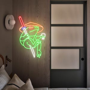 May include: A neon sign depicting a green frog wearing a straw hat and holding a sword and a glass of wine. The frog is outlined in bright green, with red, orange, and white accents. The sign is mounted on a wooden wall.