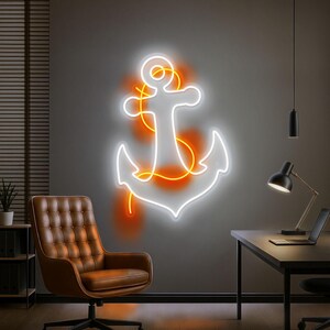 Puede incluir: Un letrero de ne&oacute;n blanco con forma de ancla con detalles en naranja est&aacute; montado en una pared gris. El letrero est&aacute; iluminado, emitiendo un brillo c&aacute;lido. Una silla de cuero marr&oacute;n y un escritorio negro con un port&aacute;til est&aacute;n en primer plano.