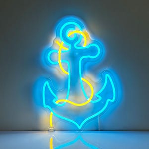 Puede incluir: Un letrero de ne&oacute;n con forma de ancla. El ancla est&aacute; delineada en azul brillante con un detalle de cuerda amarilla. El letrero est&aacute; encendido, creando un brillo vibrante sobre un fondo neutro. El tema n&aacute;utico es evidente.