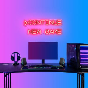 May include: A gaming setup with a black desk, monitor, and computer tower. The desk features a keyboard, mouse, and speakers. A neon sign above reads "CONTINUE NEW GAME" in pink. The background gradient transitions from pink to blue.