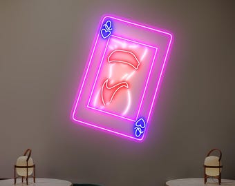 May include: A neon sign in the shape of a playing card, featuring a stylized design of a woman's body. The card is outlined in bright pink with blue accents, and the interior design is red. The sign is mounted on a neutral-colored wall.