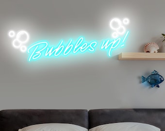 May include: A neon sign with the words "Bubbles up!" in a cursive font, illuminated in a bright turquoise color. The sign is mounted on a gray wall, with white bubble shapes on either side.