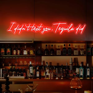 以下が含まれることがあります： バーの上に「I didn't text you, Tequila did」というフレーズが書かれた赤いネオンサイン。バーには様々な酒瓶やグラスが並び、温かく居心地の良い雰囲気を作り出しています。