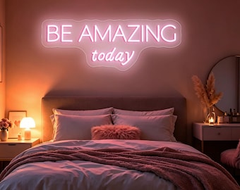 May include: A wall-mounted neon sign featuring the text BE AMAZING today in bright white light. The sign has a custom-shaped backing that follows the contour of the lettering, creating a glowing effect against the wall above a bed.