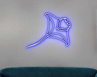 May include: A blue neon light manta ray design. The artwork features a continuous line drawing of a manta ray, emitting a bright blue glow against a gray background. The design is mounted on a wall above a teal sofa.