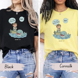 May include: Black and cornsilk t-shirts featuring a cartoon illustration of a person in a boat, a whale, and speech bubbles with the text "I'm not doing that!" and "Bet." The text "Jonah 1:3" is also included.