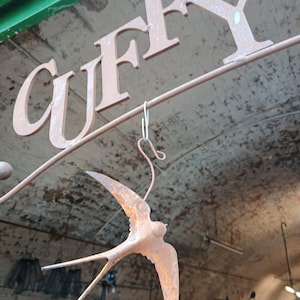May include: A rusty metal sign with the word "CUFFY" in large letters. A rusty metal bird, possibly a swallow, hangs from the sign.