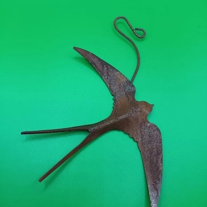 May include: A rusty metal swallow bird ornament with a loop for hanging. The bird is in flight with its wings spread out.